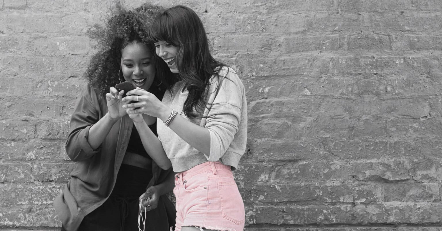 Two women laughing together while looking at a phone